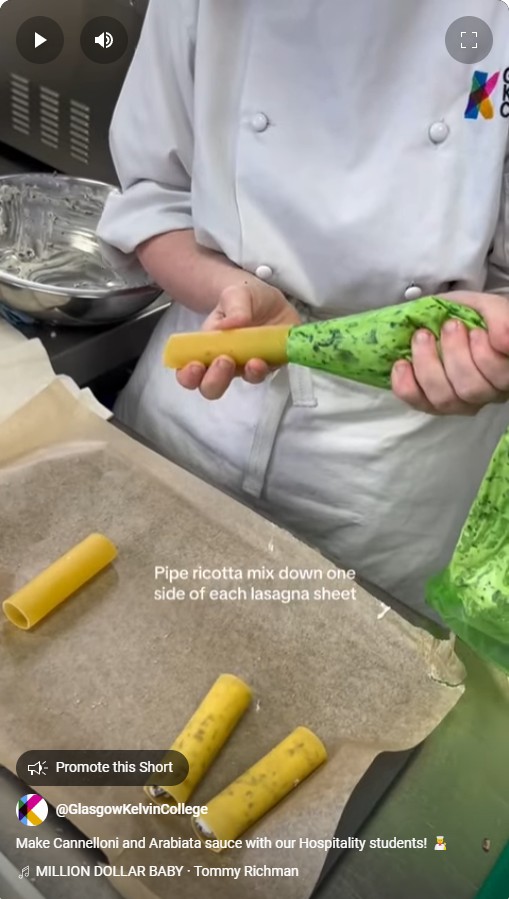 A hospitality student in a white chef's jacket pipes ricotta filling into cannelloni pasta in a professional kitchen