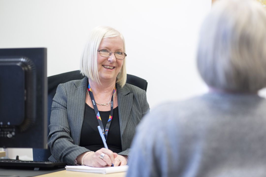 Staff member in a professional meeting at Glasgow Kelvin College, smiling and taking notes at her desk.