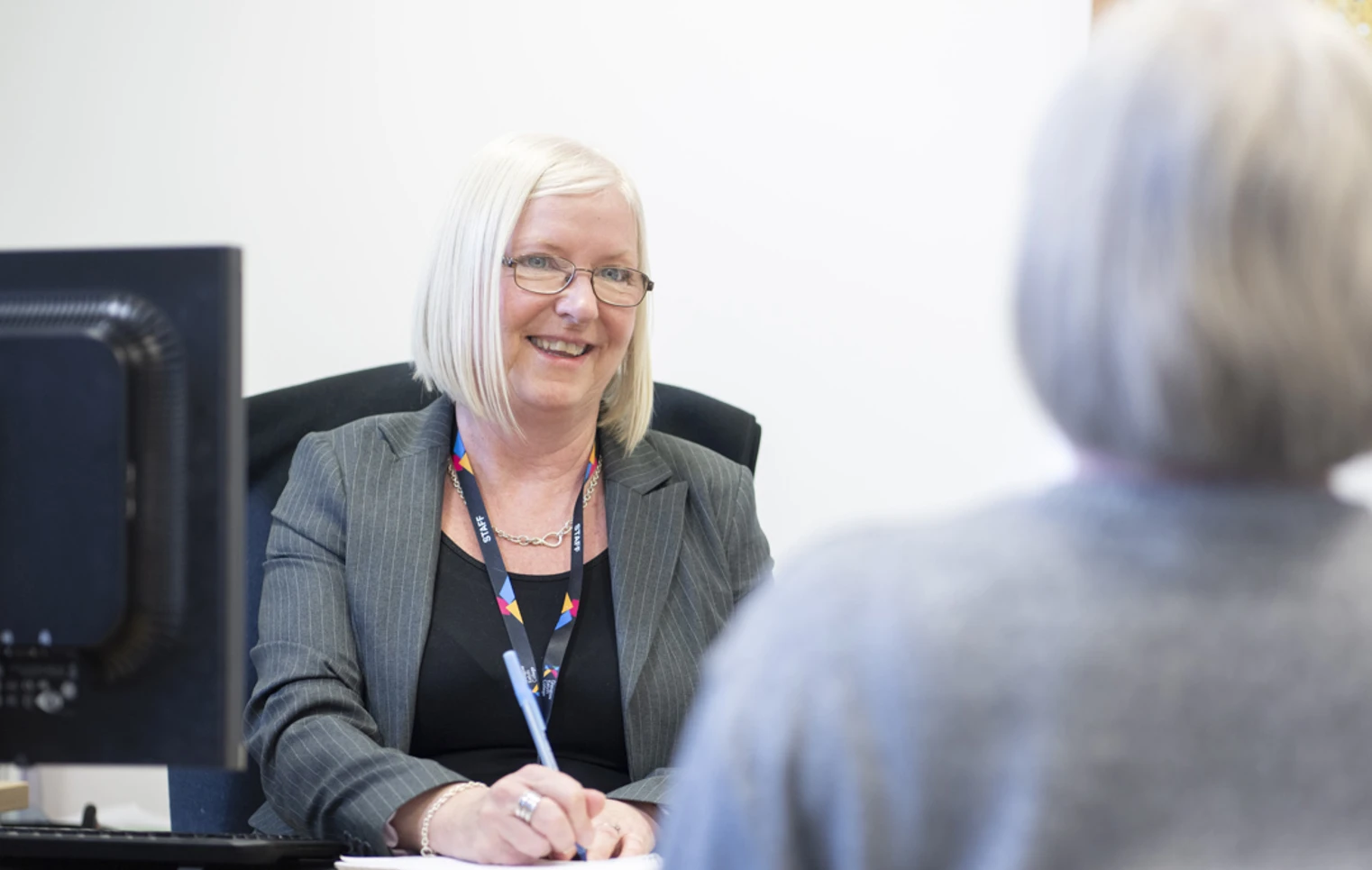 Staff member in a professional meeting at Glasgow Kelvin College, smiling and taking notes at her desk. Staff member in a professional meeting at Glasgow Kelvin College, smiling and taking notes at her desk.
