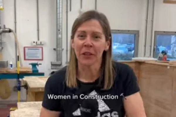 A female lecturer in a black Adidas t-shirt speaking in a joinery workshop at Glasgow Kelvin College, introducing the 'Women in Construction' course, with workbenches and tools visible in the background A female lecturer in a black Adidas t-shirt speaking in a joinery workshop at Glasgow Kelvin College, introducing the 'Women in Construction' course, with workbenches and tools visible in the background