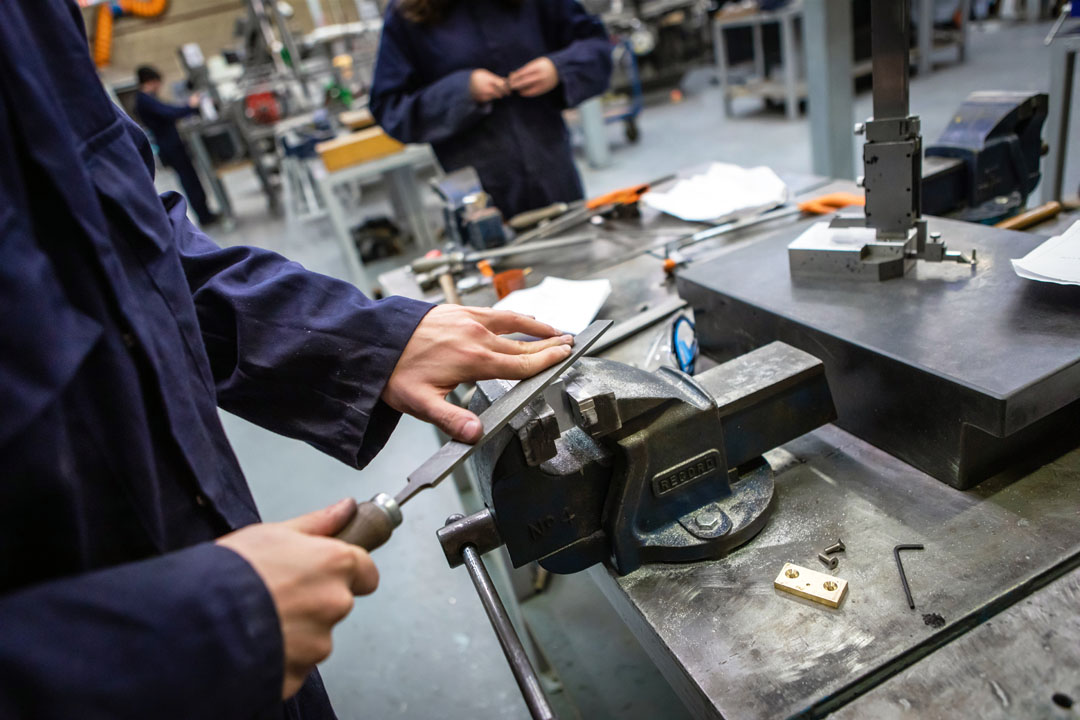 Student filing metal secured in a vice during a hands-on engineering task.
