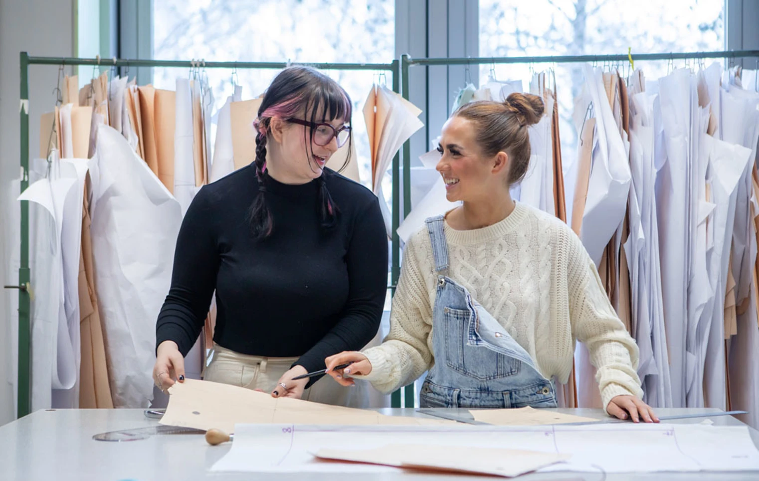 Two fashion students laughing while working on design patterns in a classroom. Two fashion students laughing while working on design patterns in a classroom.
