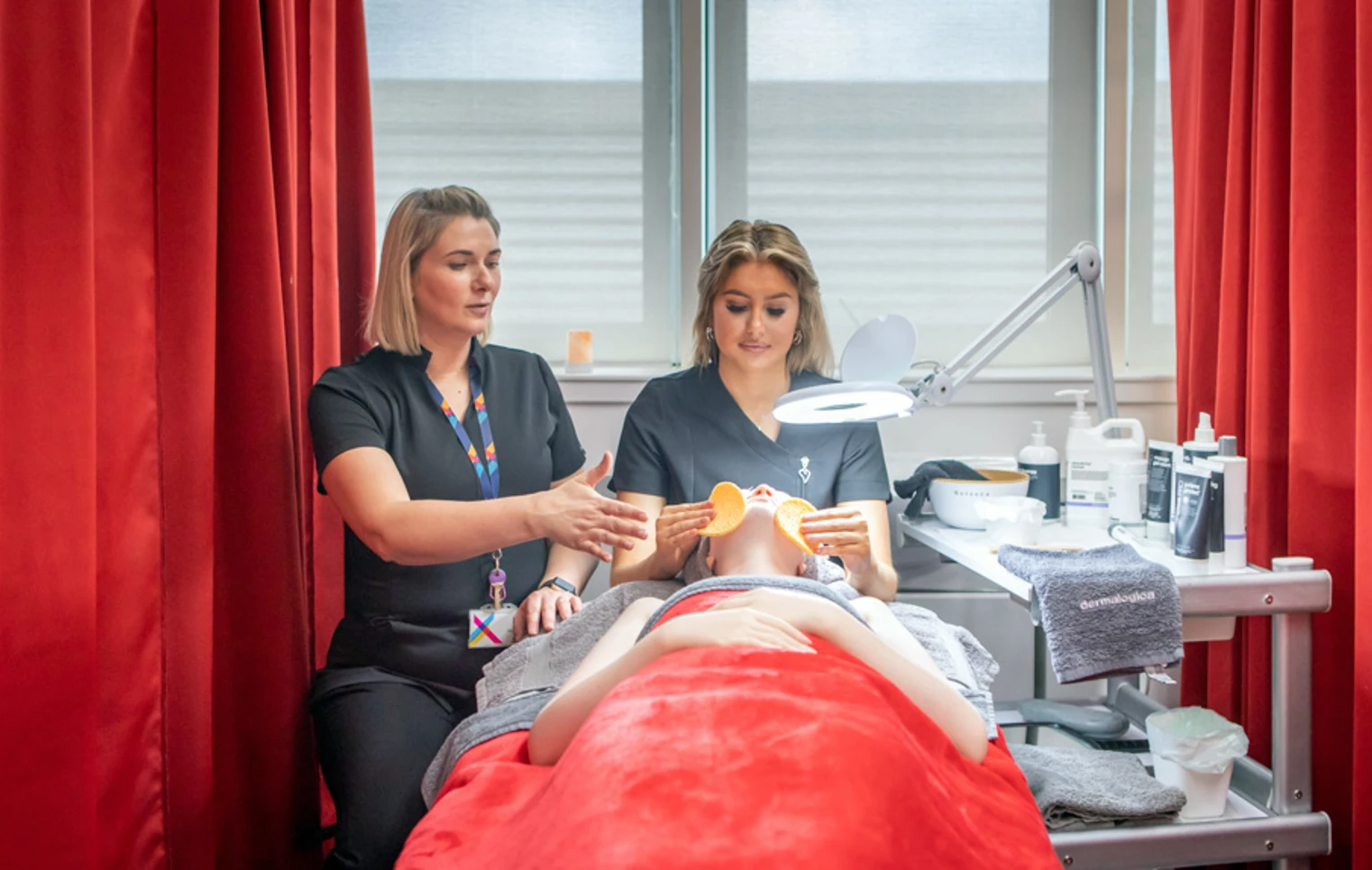 A lecturer demonstrates a facial massage technique to a beauty therapy student who is performing a treatment on a mannequin in a spa-like environment. A lecturer demonstrates a facial massage technique to a beauty therapy student who is performing a treatment on a mannequin in a spa-like environment.