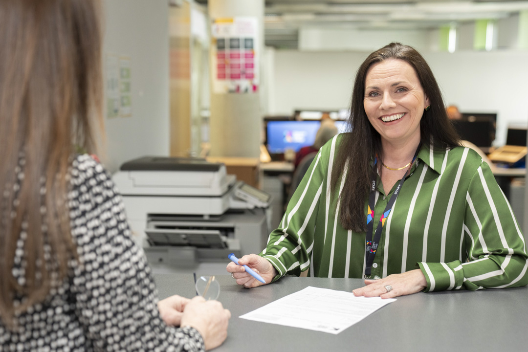 Staff member assisting a student with paperwork at a help desk in Glasgow Kelvin College