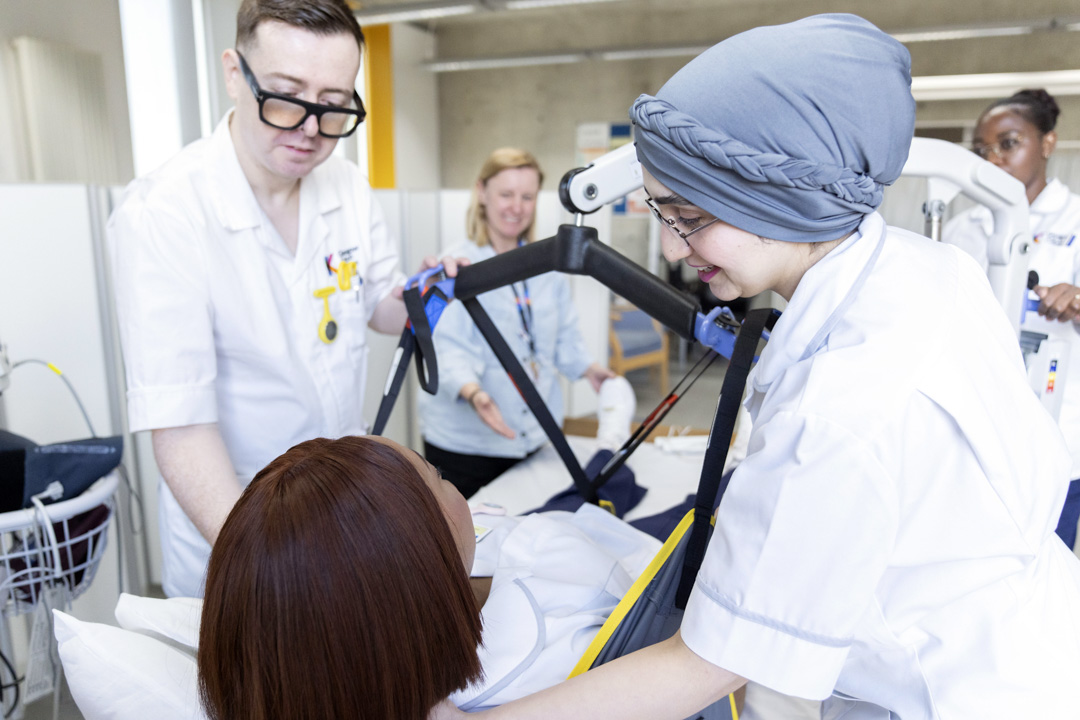 Healthcare students operate a hoist to safely move a patient in a care training session.