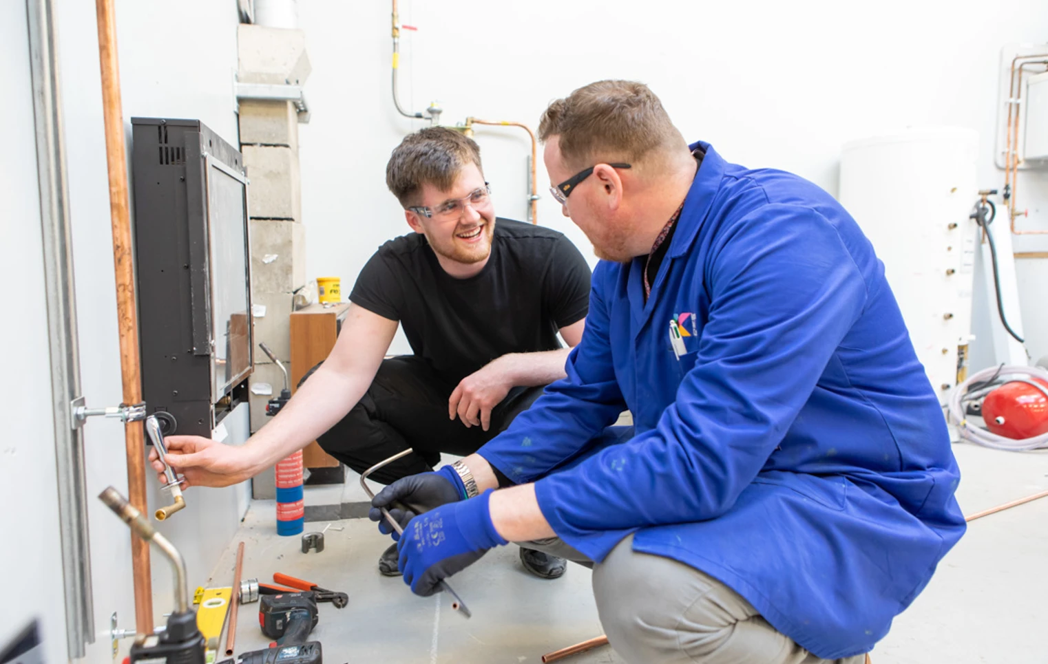 A plumbing lecturer and student smiling and collaborating closely while working together to install copper piping in a practical training session. A plumbing lecturer and student smiling and collaborating closely while working together to install copper piping in a practical training session.