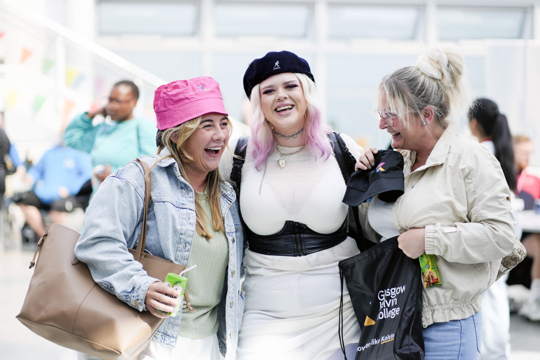 Three students laughing and smiling at the Glasgow Kelvin College Open Day, holding branded tote bags