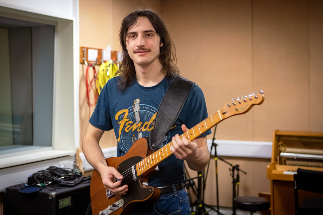 A guitarist smiling while playing a Fender Telecaster in a practice room.
