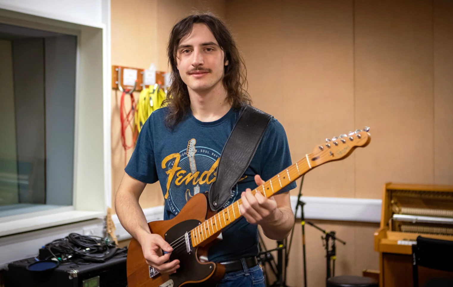 A guitarist smiling while playing a Fender Telecaster in a practice room. A guitarist smiling while playing a Fender Telecaster in a practice room.