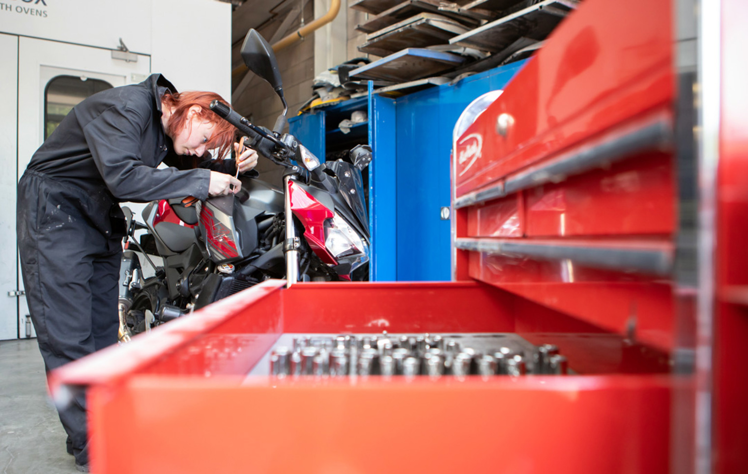 Student repairing a motorcycle beside a red tool chest in the automotive workshop.