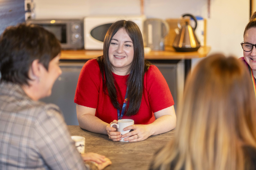 Support staff at Glasgow Kelvin College enjoying a relaxed conversation over coffee in a staff kitchen area.