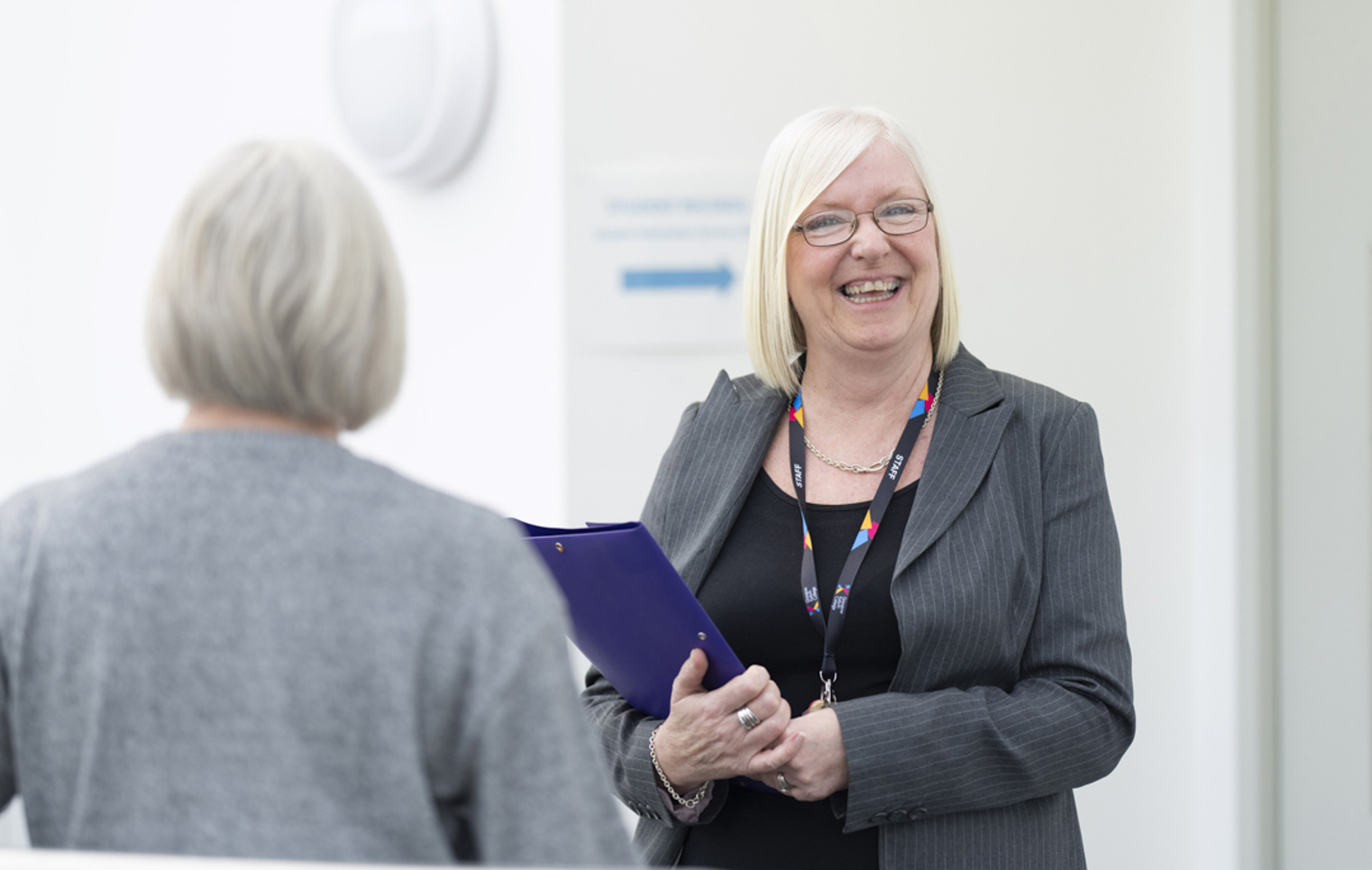 Pauline from Glasgow Kelvin College’s Finance team smiling and holding a folder while speaking with a colleague in a bright office space