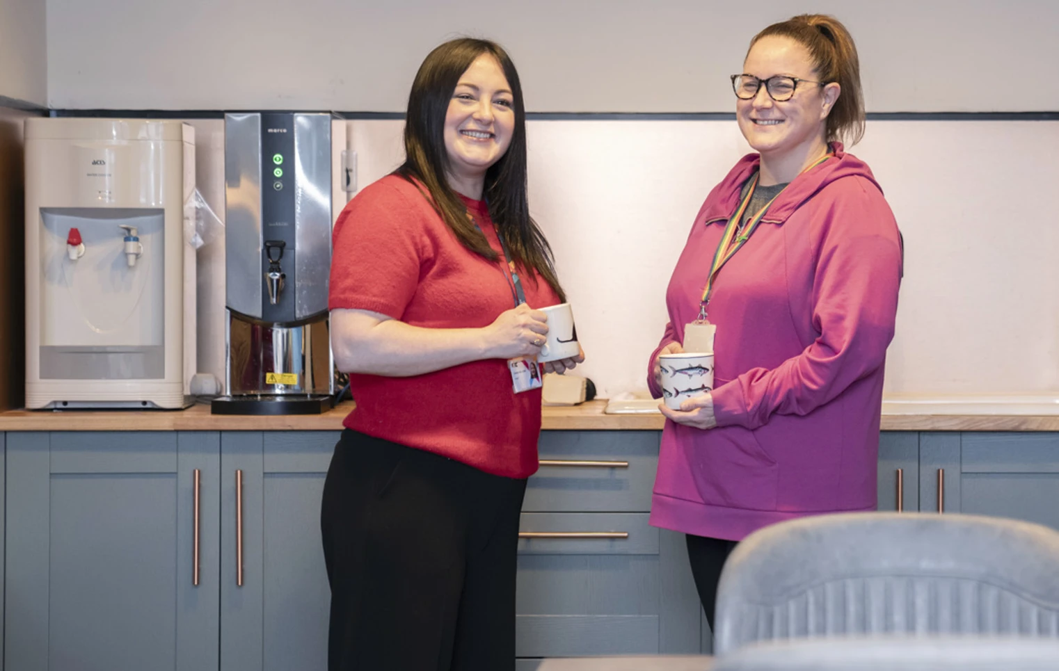 Two Glasgow Kelvin College staff members smiling and chatting over mugs in a staff kitchen area Two Glasgow Kelvin College staff members smiling and chatting over mugs in a staff kitchen area