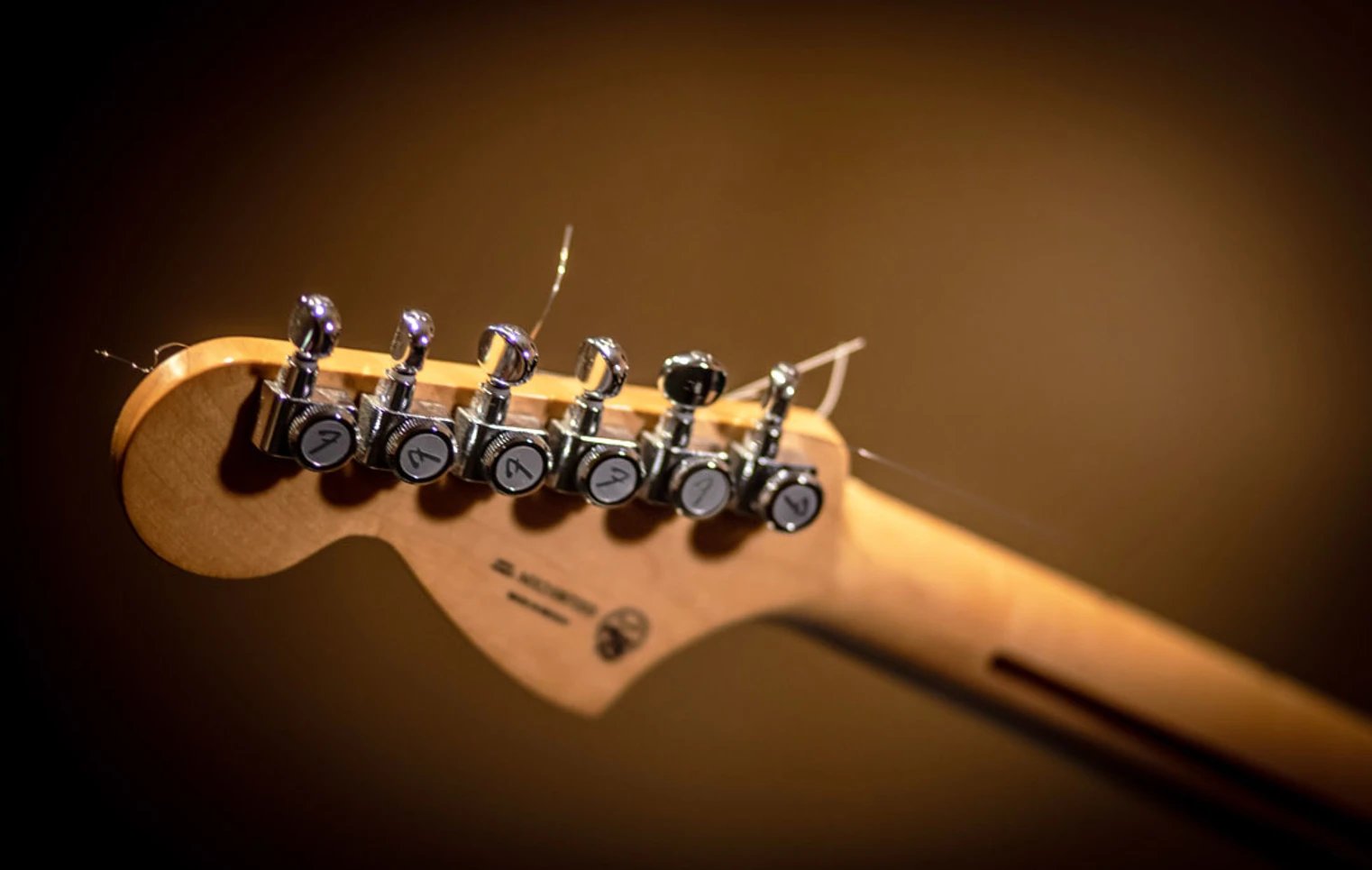 A wooden guitar headstock with chrome tuning pegs and loose strings, set against a blurred background. A wooden guitar headstock with chrome tuning pegs and loose strings, set against a blurred background.