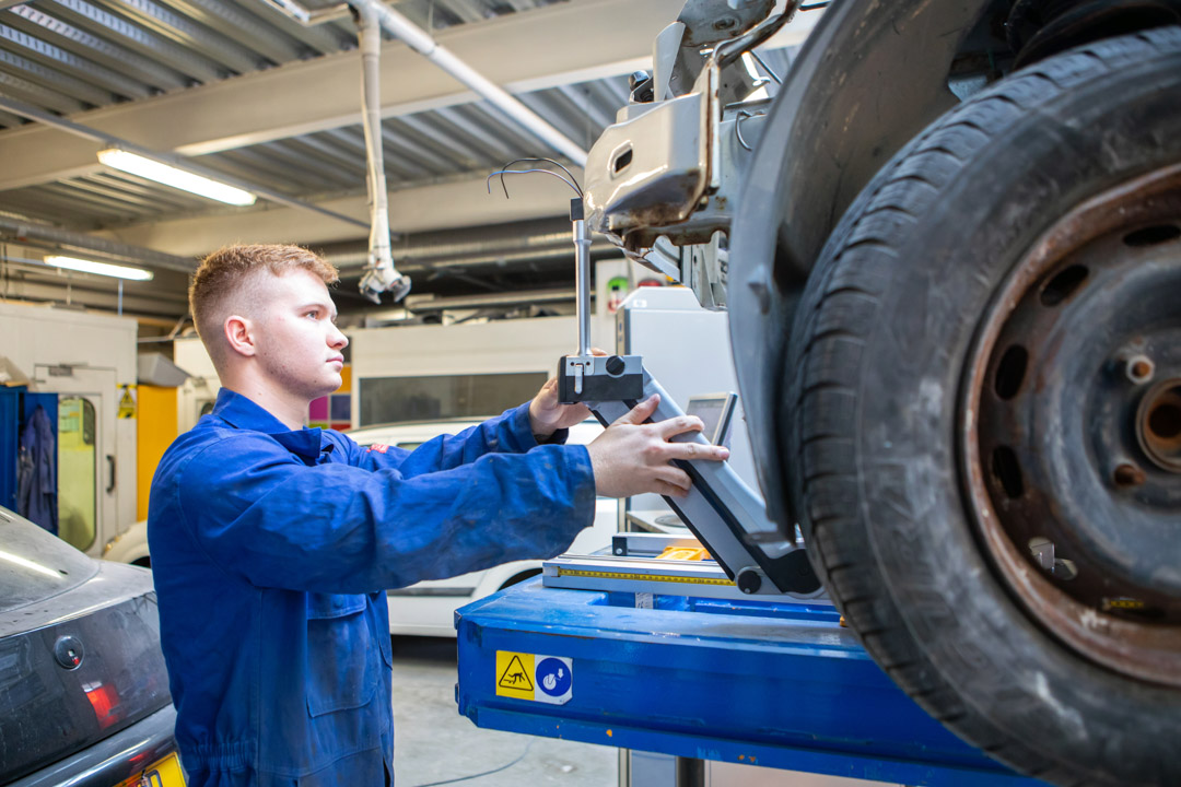 Automotive student adjusting alignment tools on a raised vehicle during a practical class.