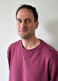 Portrait of Louis Rive wearing a burgundy sweatshirt against a plain background.