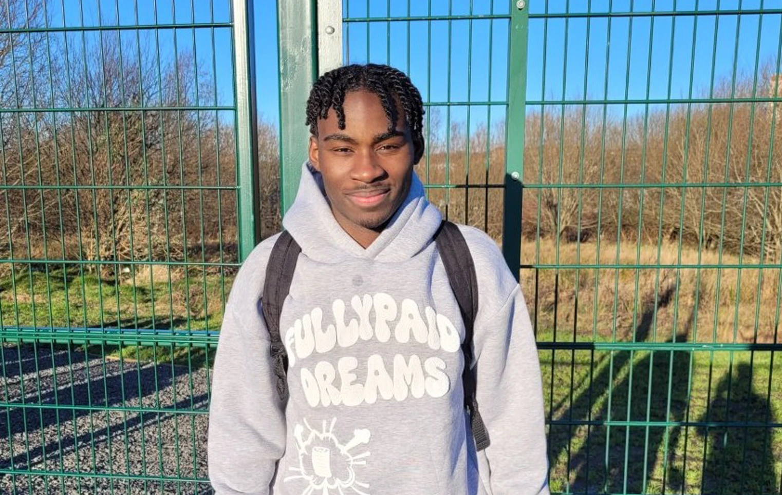 Glasgow Kelvin College student Tuacenio Santos standing outside on a sunny day in sportswear, holding headphones and a water bottle, smiling at the camera. Glasgow Kelvin College student Tuacenio Santos standing outside on a sunny day in sportswear, holding headphones and a water bottle, smiling at the camera.