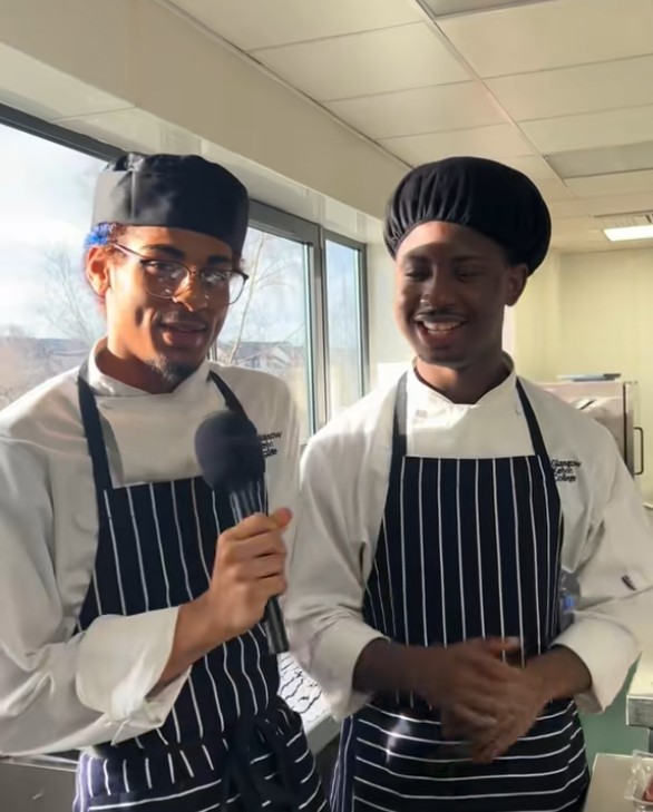 Hospitality students in chef uniforms speaking into a microphone in a professional kitchen at Glasgow Kelvin College.